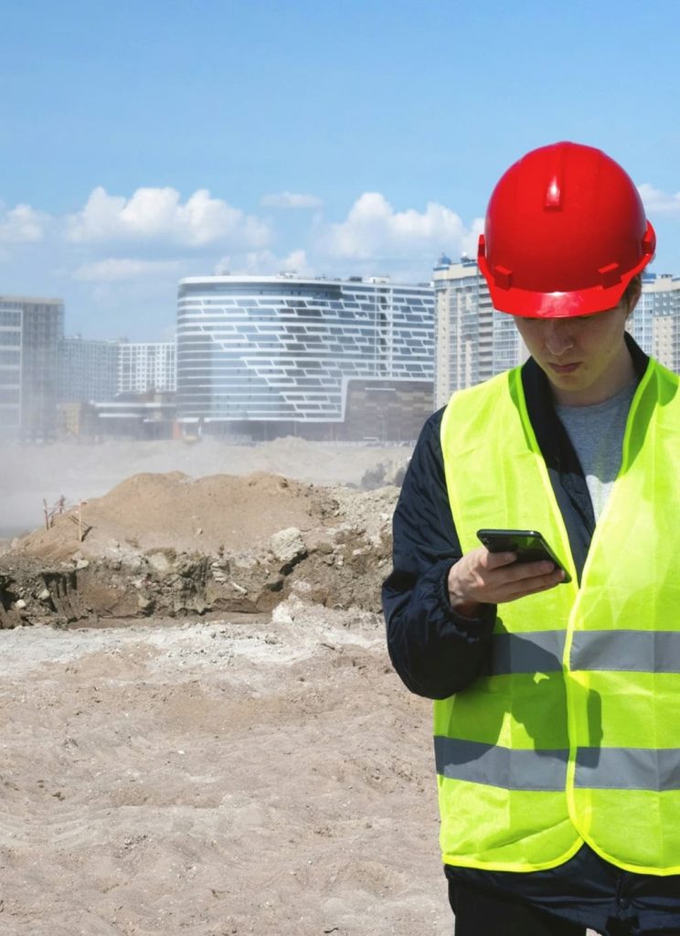 Fachkraft prüft Baustelle mit Helm und Smartphone